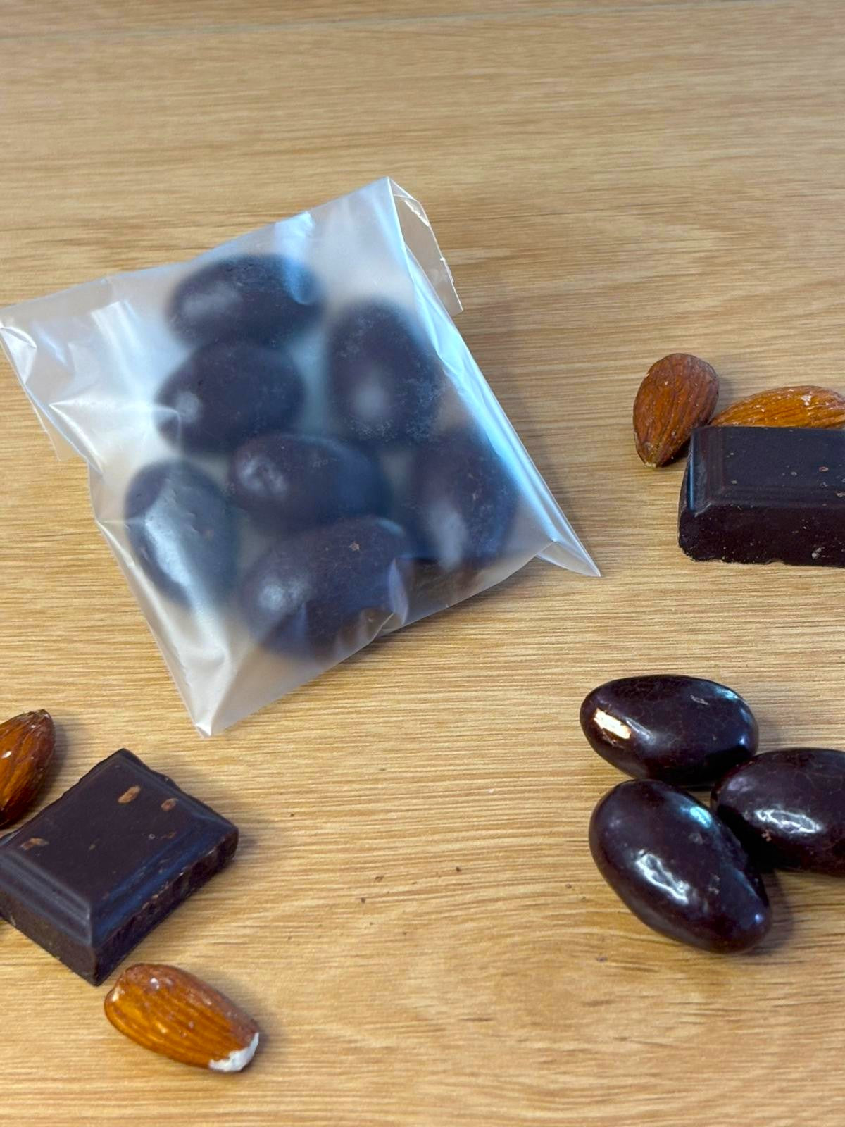 Illustration d'un sachet de 30 grammes d'amandes grillées enrobées de chocolat noir entouré d'amandes grillées et de carreaux de chocolat noir
